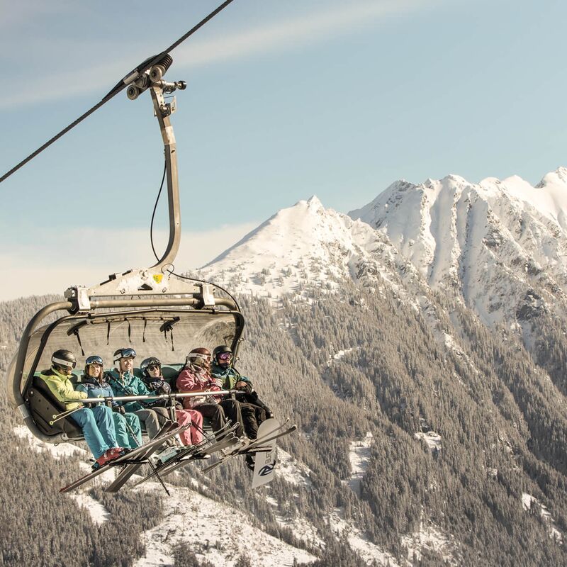 Skifahrer am Sessellift genießen den Blick auf die verschneiten Berge.