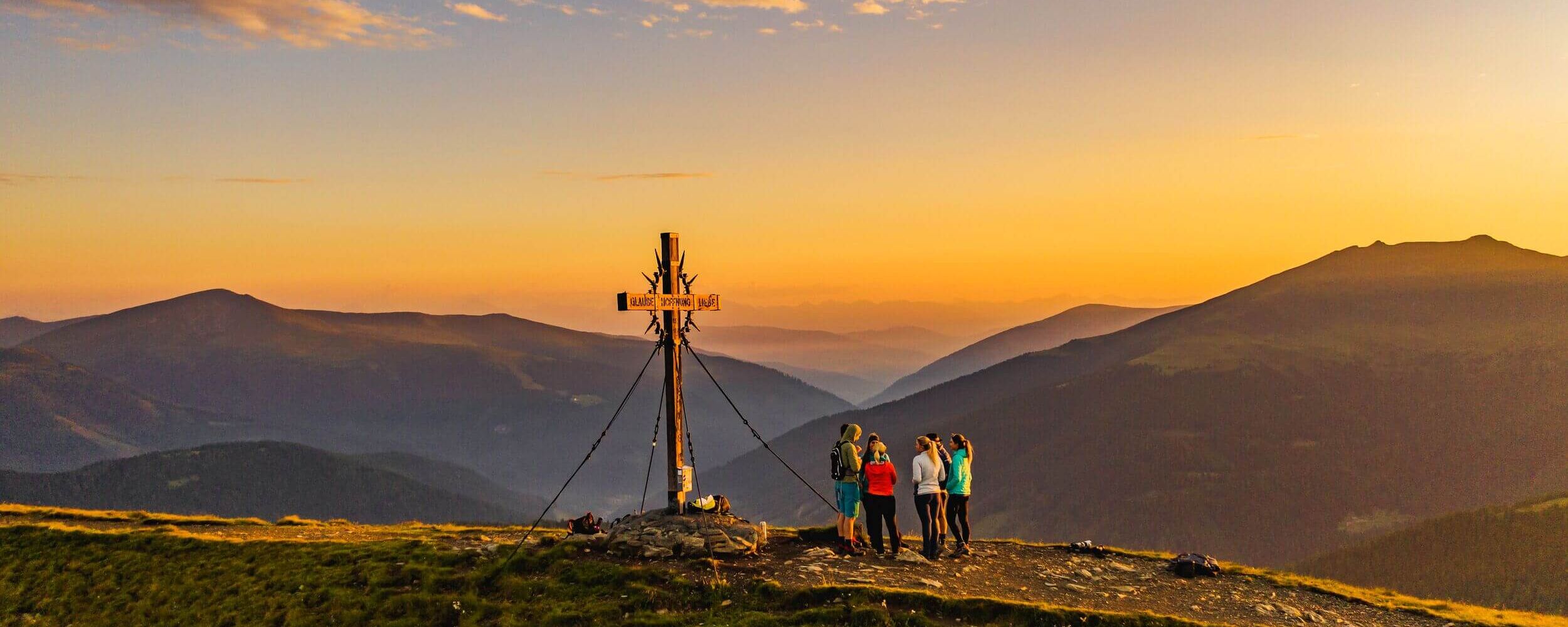 Gipfelkreuz mit Wandergruppe bei Sonnenuntergang in Kärnten