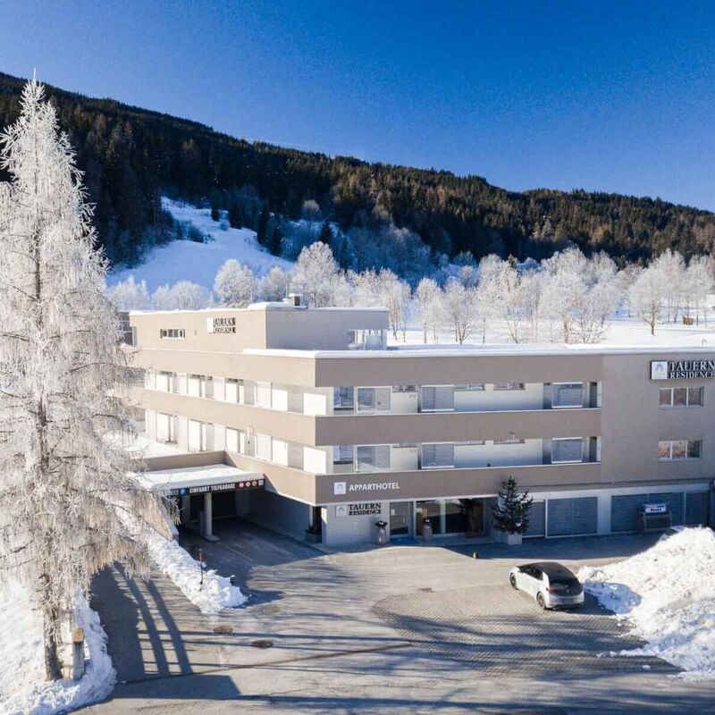 Winterliche Aussicht auf das moderne Aparthotel inmitten schneebedeckter Landschaft und verschneiter Bäume.
