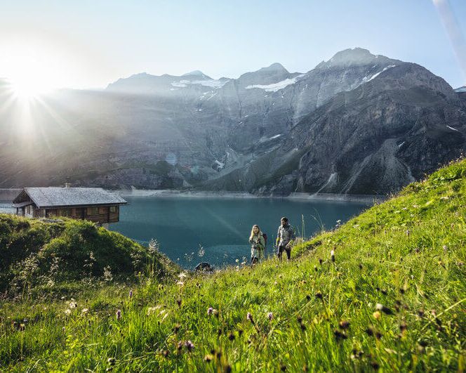 A hiker at the upper Kaprun high mountain reservoir, surrounded by high-alpine terrain.