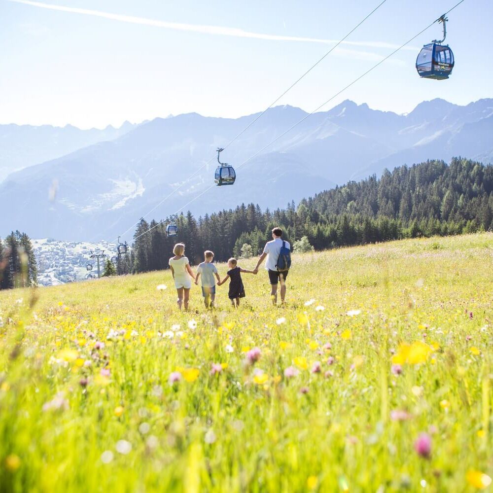Een familie wandelt over een bergweide terwijl boven hen een gondellift gemakkelijk toegang geeft tot het wandelgebied