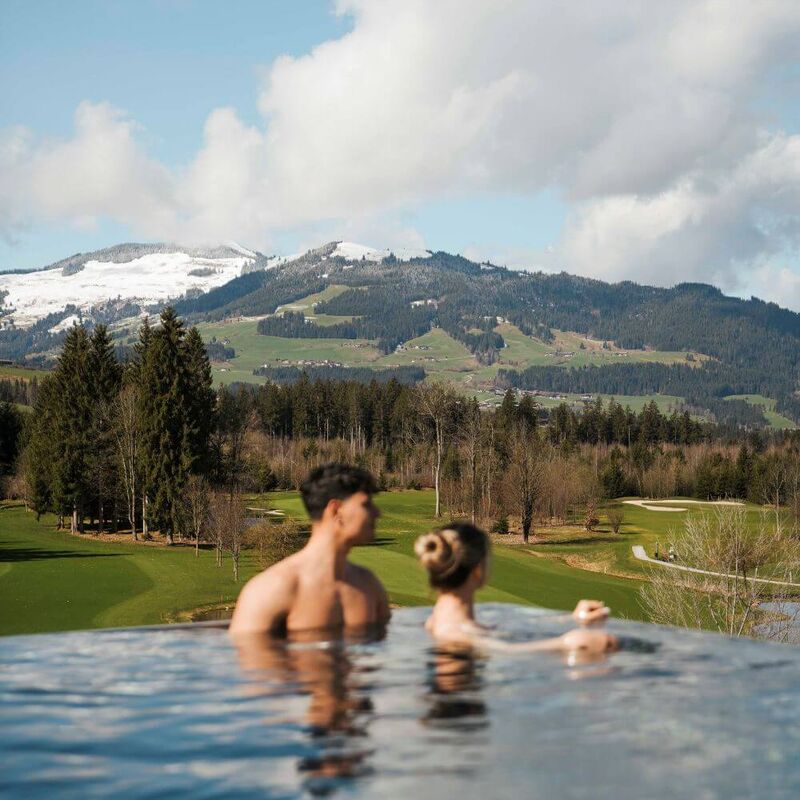 Pärchen schwimmt im Außenpool auf der Dachterrasse und blickt auf den angrenzenden Golfplatz