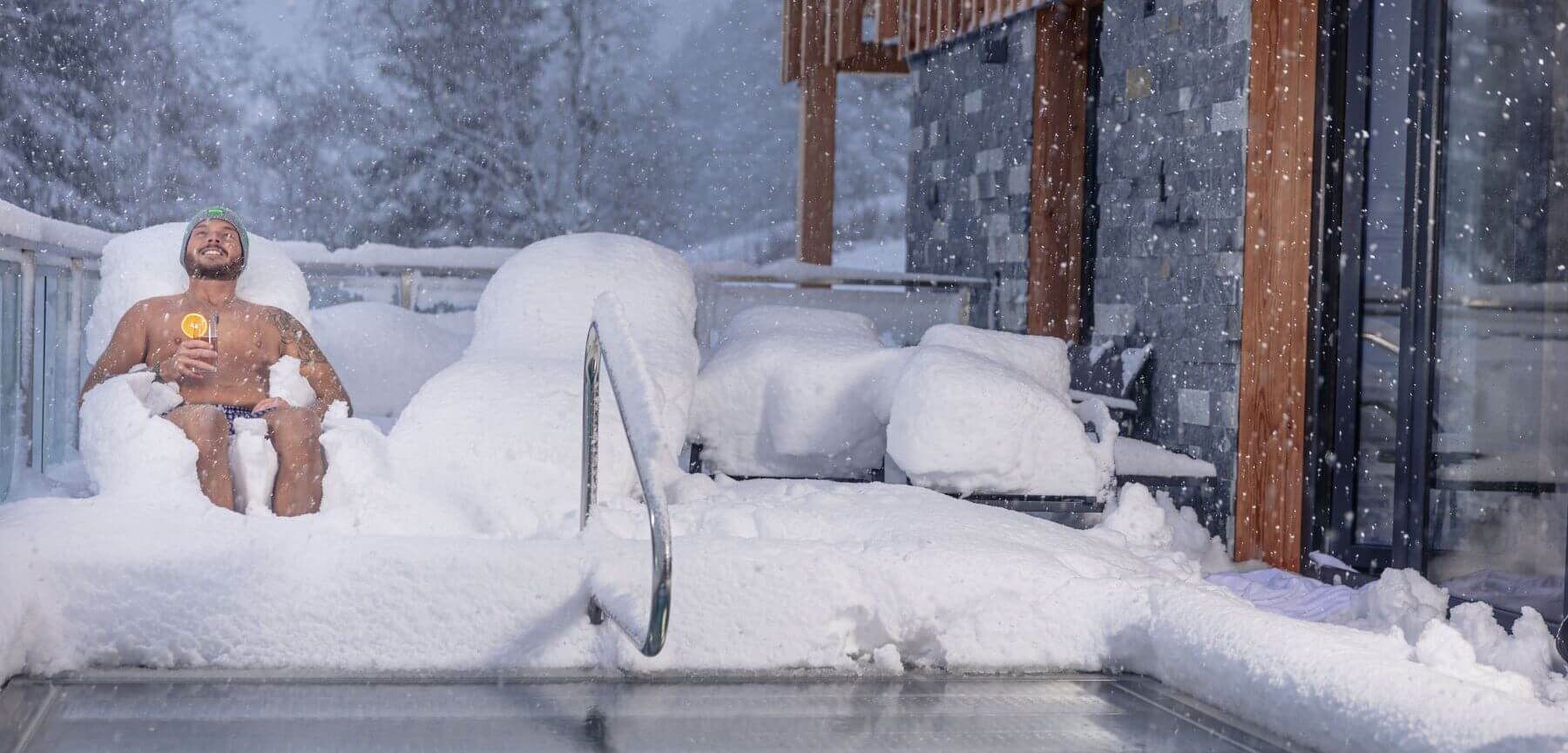 Ein Mann liegt am privaten Pool im Ferienhaus und freut sich über den Schneefall.