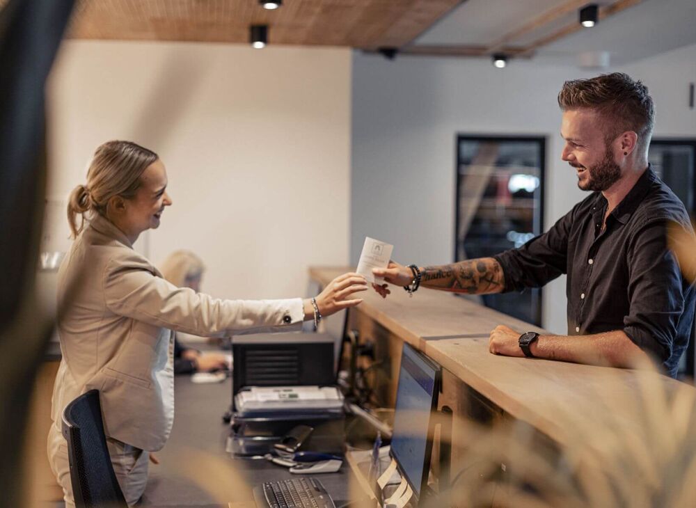 A receptionist hands her guest a key card.