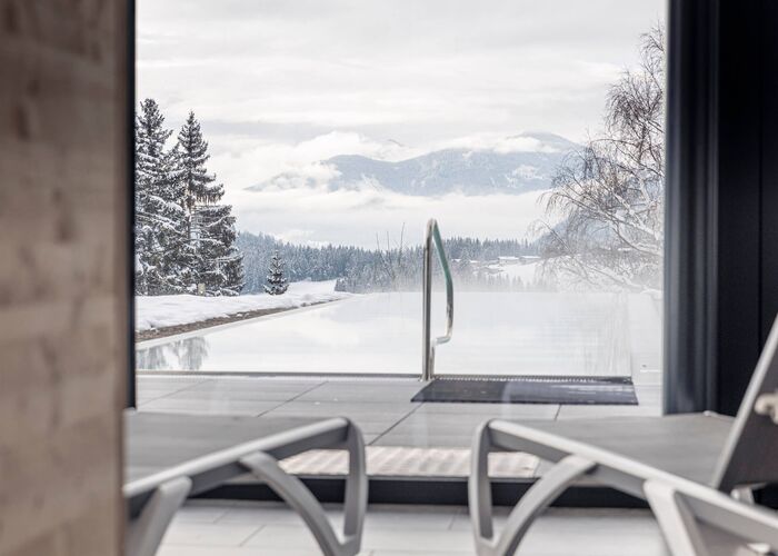 Ruheraum mit Liegen und Blick auf den beheizten Außenpool sowie die verschneite Berglandschaft im Hideaway Dachstein West