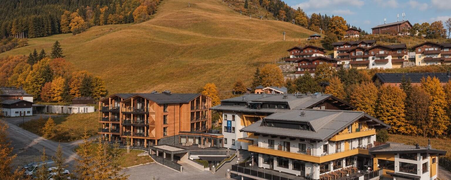 Herbstliche Aussicht auf die Saalbach Suites mit bunten Bäumen und sanften Hügeln im Hintergrund.