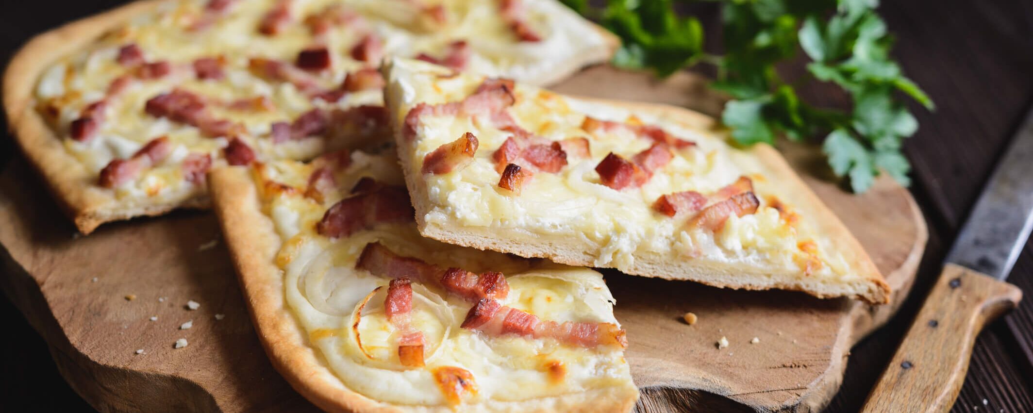Delicious flammkuchen with bacon and onions, served on a wooden board with fresh herbs.