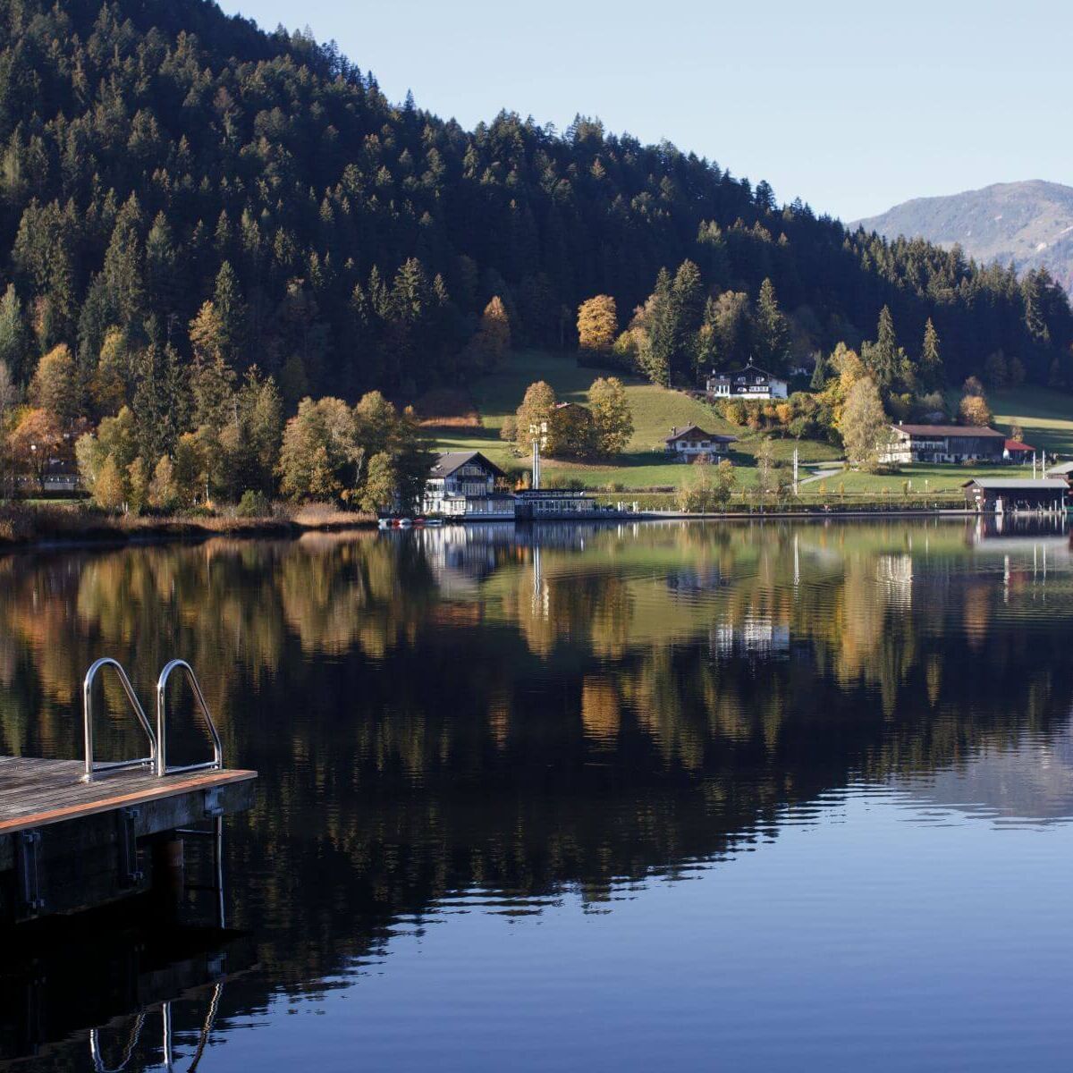 A tranquil mountain lake in Tyrol reflects the surrounding forests and majestic peaks in the clear water in the early morning