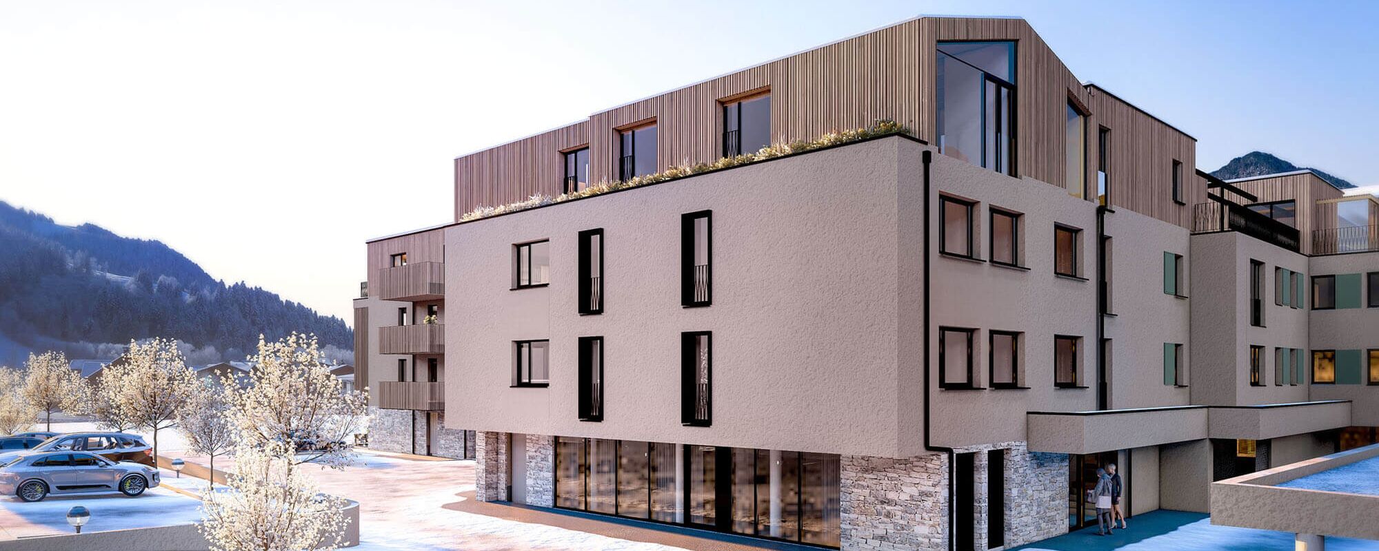 Modern appartementencomplex met sneeuwbedekte grond en bomen, gelegen in een bergachtige omgeving.