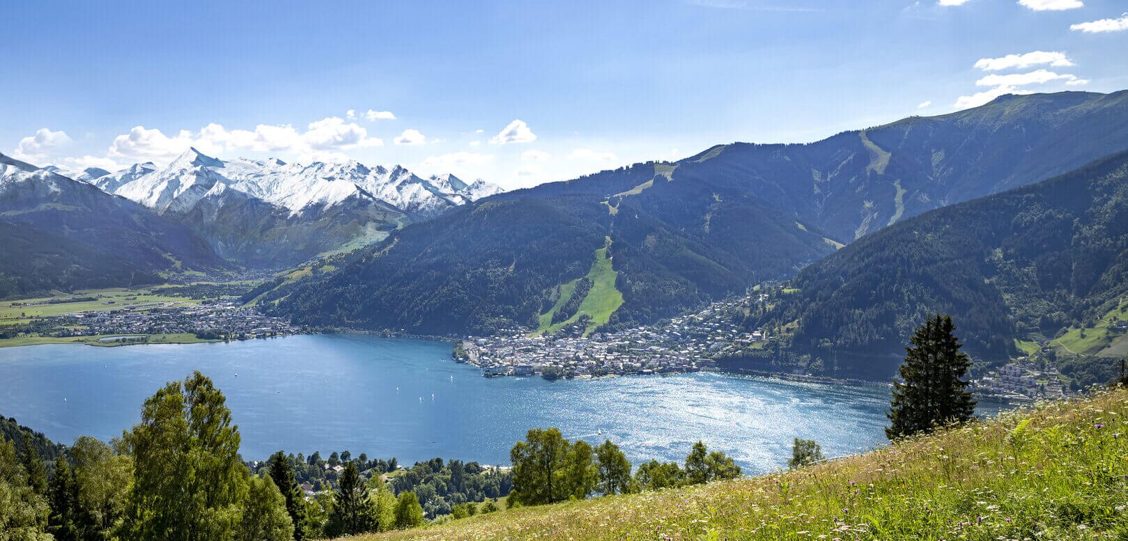 Der Zeller See eingebettet zwischen Bergen, dem Kitzsteinhorn Gletscher, blühenden Wiesen und der Stadt Zell am See.