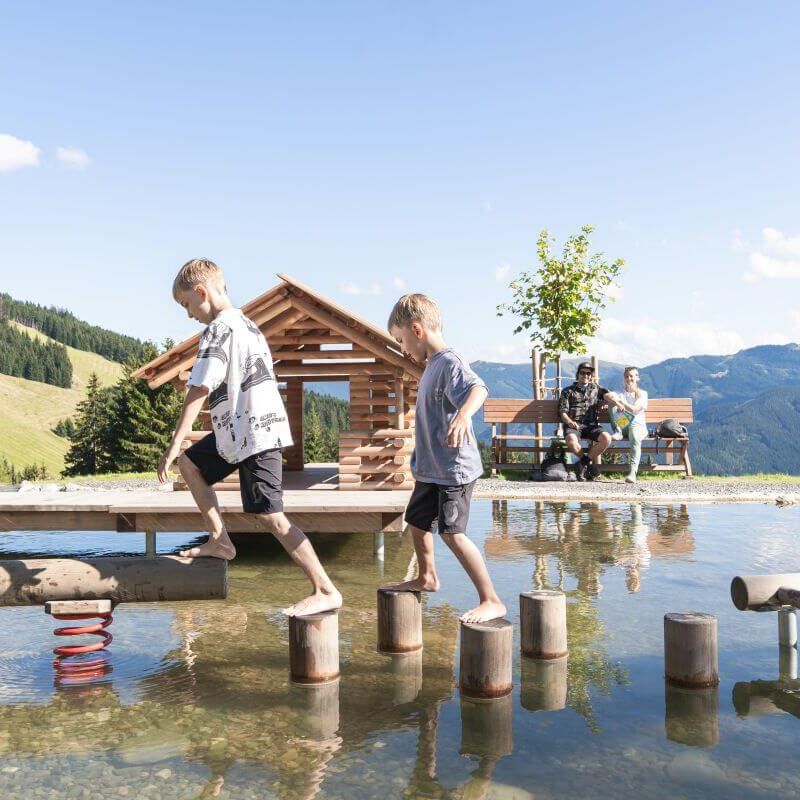 Two children balance on wooden elements in the water.