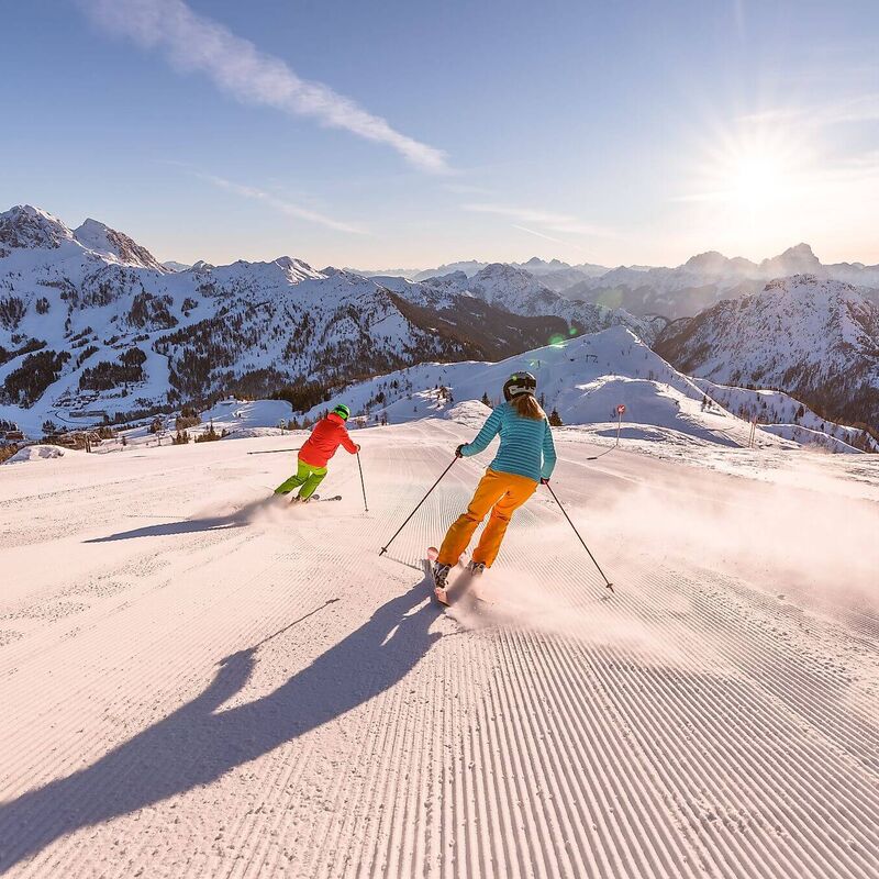 2 Skifahrer genießen Sonnenskilauf auf perfekten Pisten am Nassfeld/Kärnten mit Blick auf den Gartnerkofel.