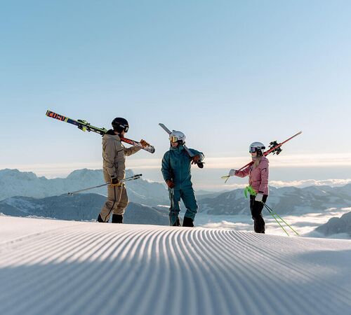 3 Skifahrer Freunde stehen auf der frischen Piste oberhalb des Nebelmeers in der Sonne.