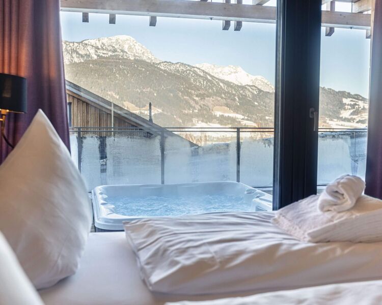 Blick auf einen Whirlpool und die Berge von einem modernen Schlafzimmer mit gemütlicher Atmosphäre.