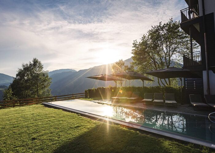 Außenpool des Hideaway Dachstein West mit Liegen, Sonnenschirmen und Blick auf die Berge bei Sonnenuntergang.