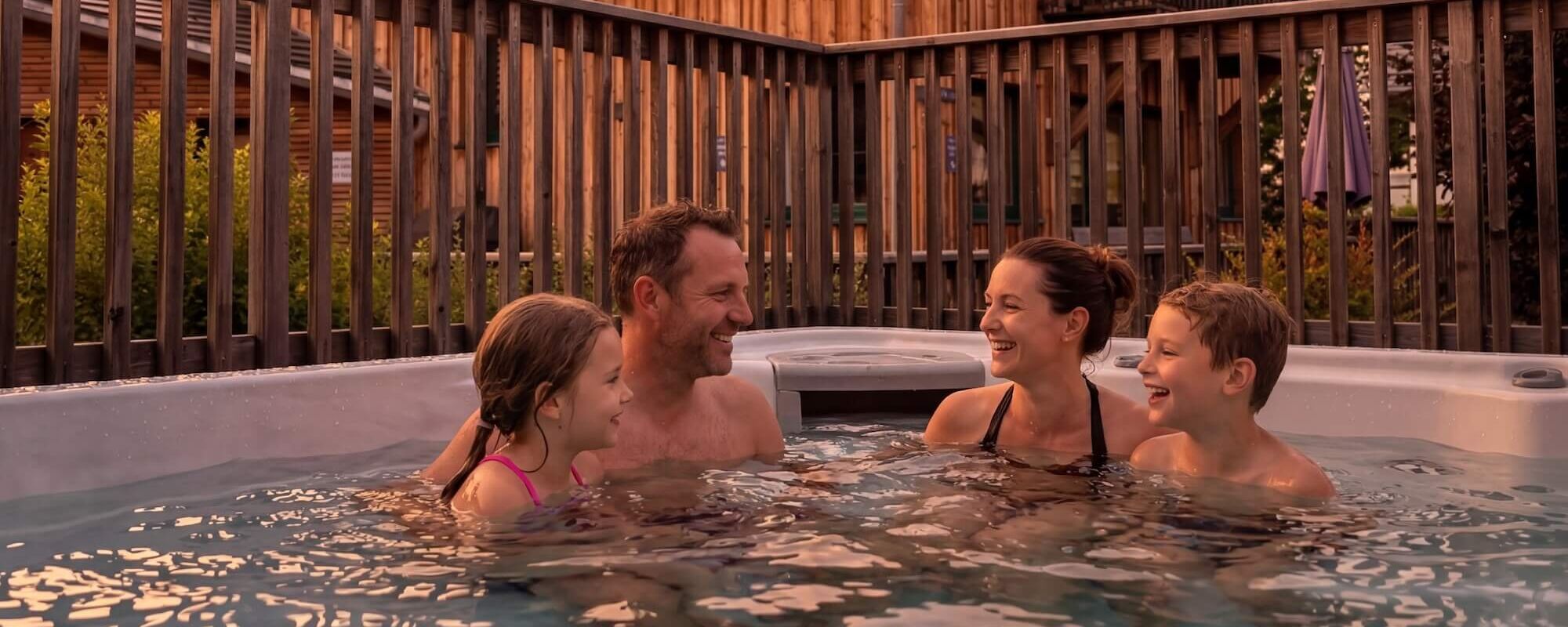 A family enjoys relaxing in a hot tub at an alpine resort during a beautiful sunset.
