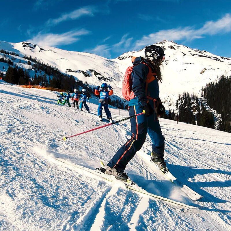Skilehrerin übt Pflugbögen mit einer Kindergruppe auf der Piste