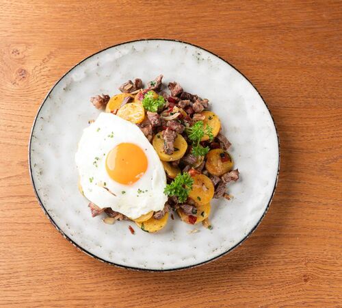 Plate with Tyrolean Gröstl and fried egg on a kitchen table