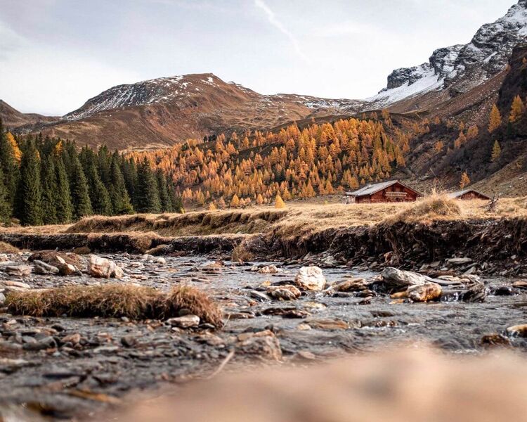 Herbstliche Landschaft in Rauris mit bunten Laubbäumen, steilen Bergen und einem klaren Fluss im Vordergrund.