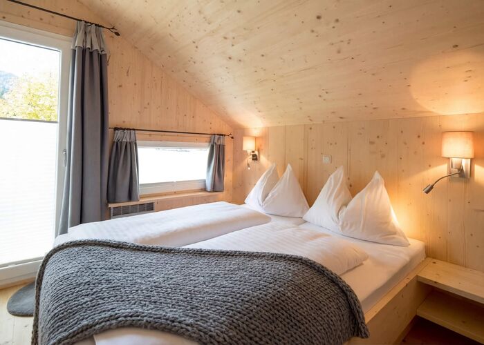 Cozy wooden bedroom with twin beds, soft blankets, and large windows showcasing a serene lakeside view.