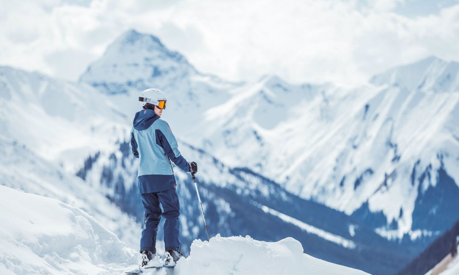 Skifahrer steht am Pistenrand im Tiefschnee und genießt den Ausblick auf die verschneiten Berge und Täler