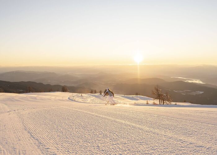 Eine Skifahrerin fährt über die breite Skipiste der Gerlitzen Alpe, umgeben von einem beeindruckenden Panorama.