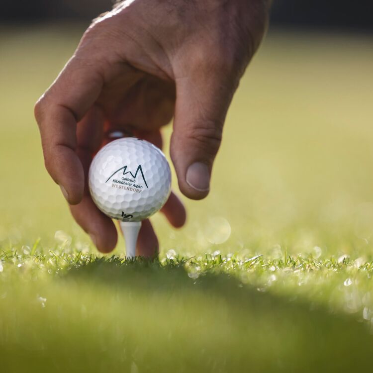 Eine Hand platziert einen Golfball sanft auf dem grünen Gras im Golfclub Kitzbüheler Alpen.