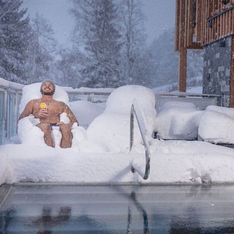 Ein Mann liegt am privaten Pool im Ferienhaus und freut sich über den Schneefall.