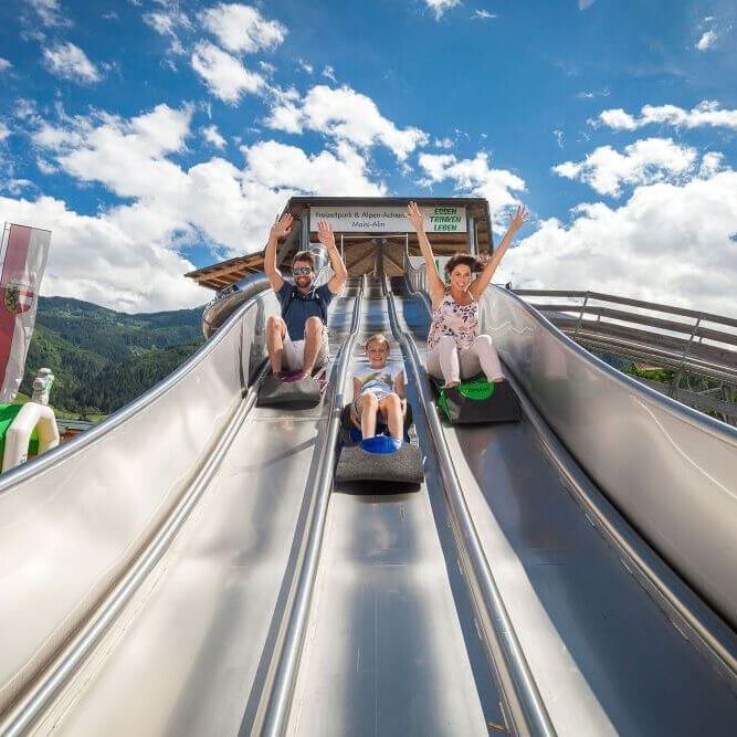 Families enjoy a thrilling ride down the slides at Familienpark Maiskogel under a bright blue sky. | © Kitzsteinhorn
