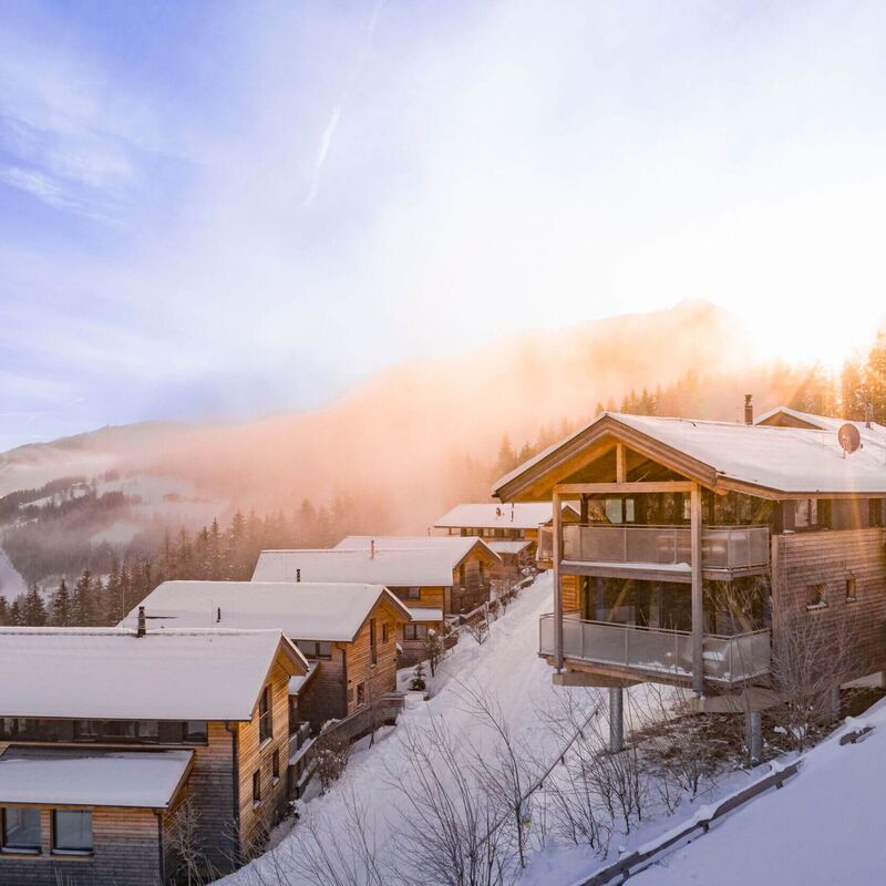 Ferienhäuser und Chalets in winterlich verschneiter Landschaft und Sonnenaufgang