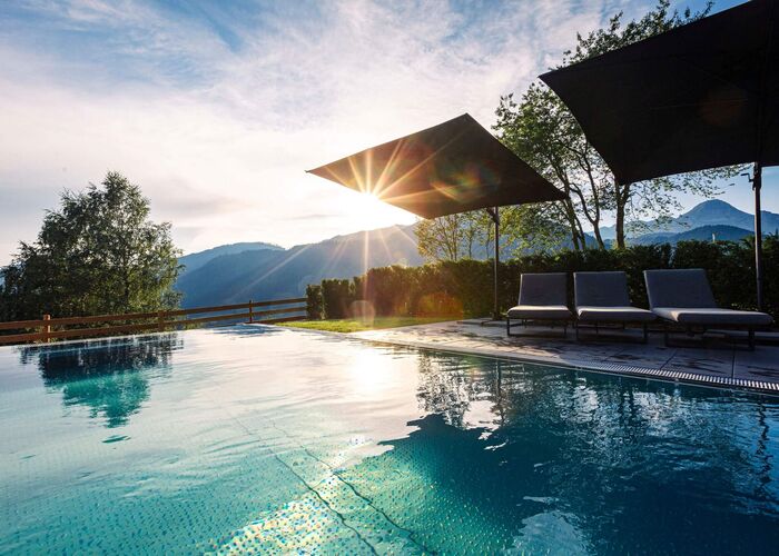 Außenpool im Hideaway Dachstein West mit Liegen, Sonnenschirmen und Blick auf die Berglandschaft bei tief stehender Sonne.
