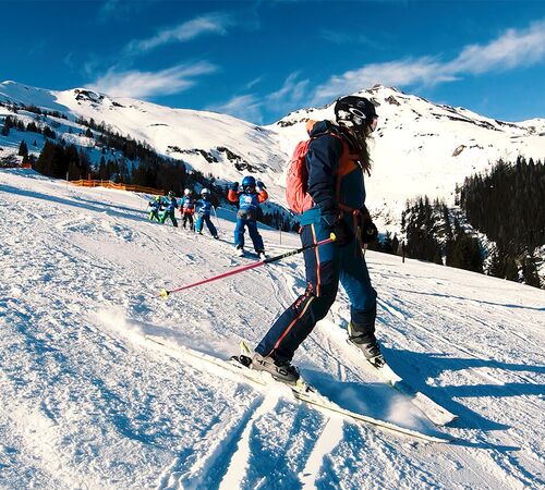 Skilehrerin übt Pflugbögen mit einer Kindergruppe auf der Piste