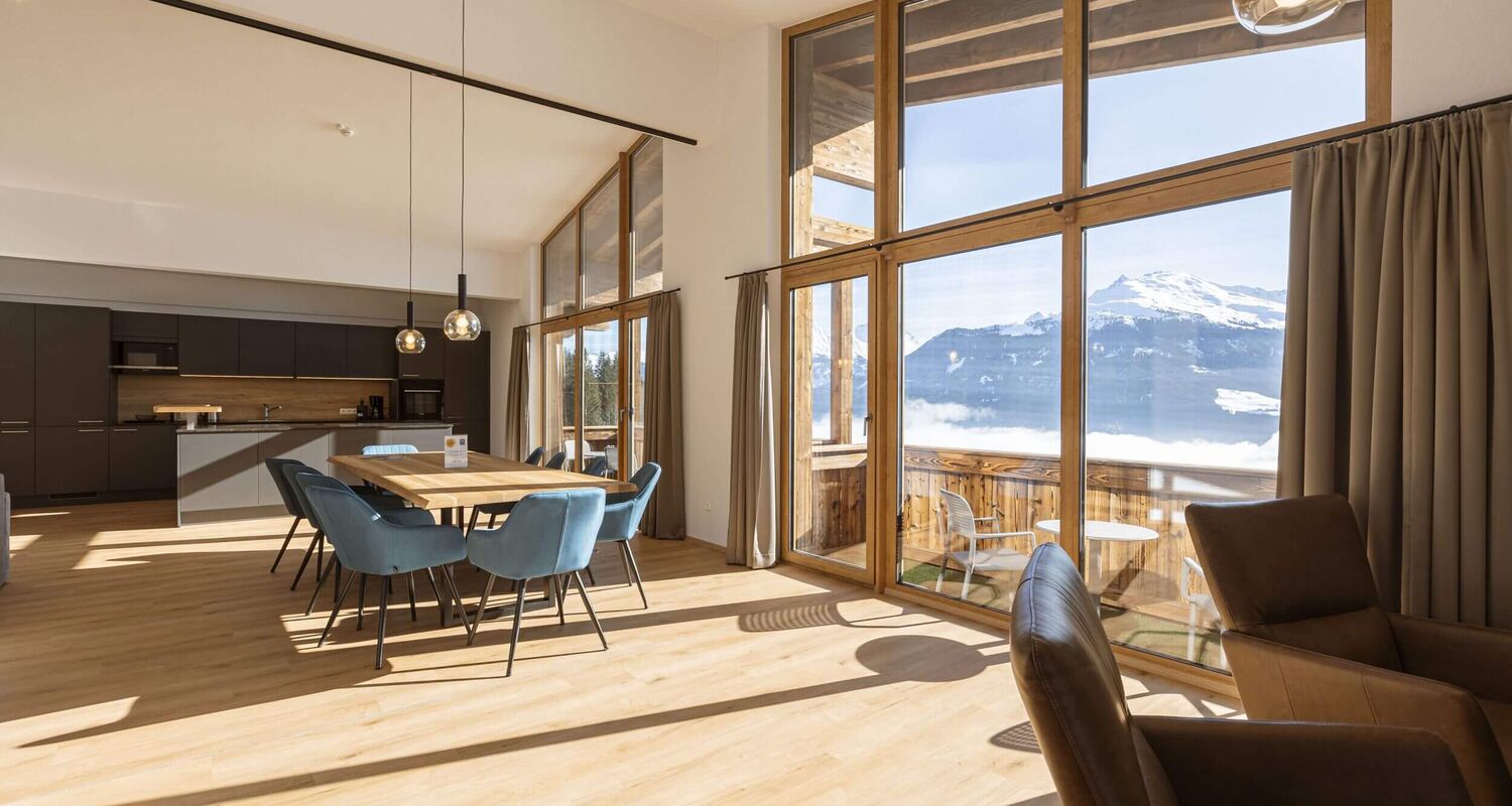 Spacious living area with a dining table and stunning mountain views through large windows.