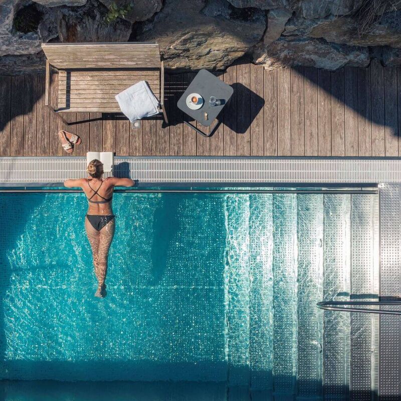A young woman lies in the private pool of her chalet, reading a book