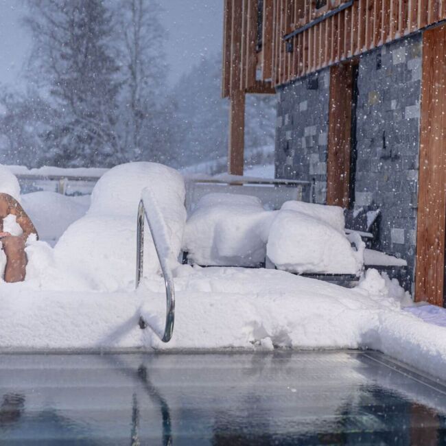 Ein Mann liegt am privaten Pool im Ferienhaus und freut sich über den Schneefall.