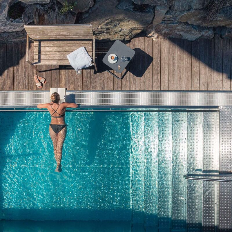 Eine Frau entspannt im Wellness-Pool, während Möbel auf der Holzterrasse bereitstehen.