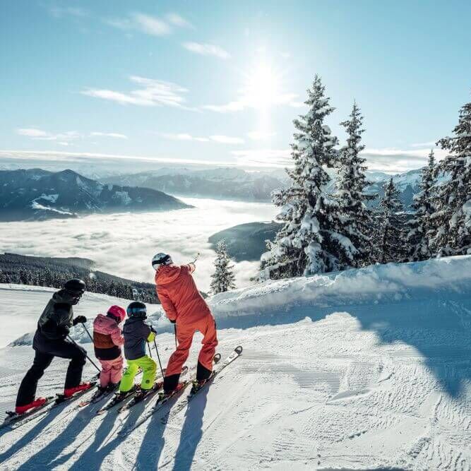 A family enjoys skiing on a snowy slope with stunning mountain views at Schmittenhöhe.