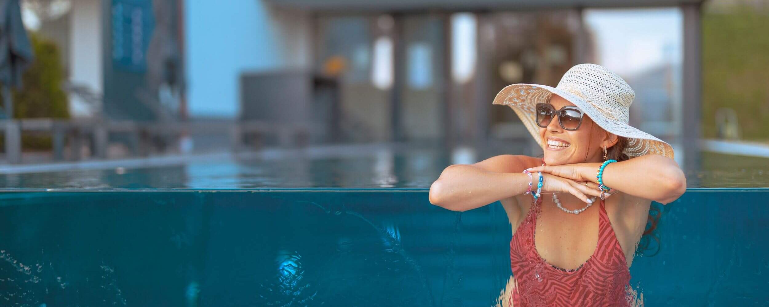 Frau schwimmt bei sonnigen Wetter im Infinity Pool eines Ferienresorts