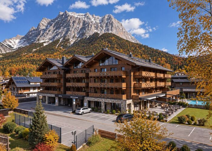 Buitenaanzicht van Bergresort Zugspitze Ehrwald in de herfst, omgeven door kleurrijke herfstnatuur en het indrukwekkende Tiroolse berglandschap rond de Zugspitze.