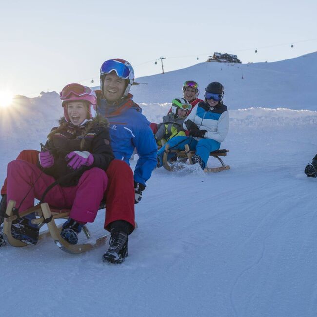 Freunde mit Kindern und 4 Schlitten auf einer Rodelpiste