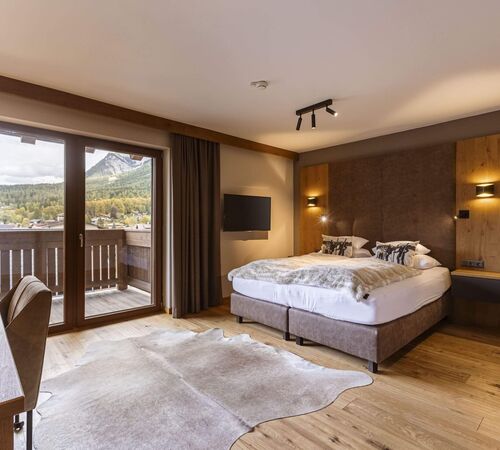 Boxspring Doppelbett mit gemütlichen Bettdecken in einem alpinen Schlafzimmer mit Balkon und grandioser Aussicht auf die Natur