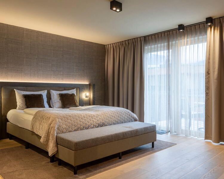 Doppelbett mit Polsterbank und bodentiefem Fenster im Doppelzimmer im Bergresort Westendorf