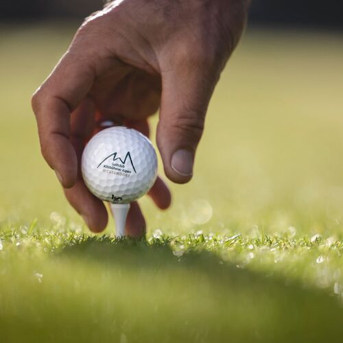 Eine Hand platziert einen Golfball sanft auf dem grünen Gras im Golfclub Kitzbüheler Alpen.
