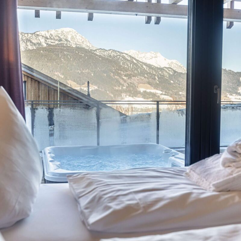 A luxurious view of a whirlpool on a balcony, framed by mountains and soft bedding.