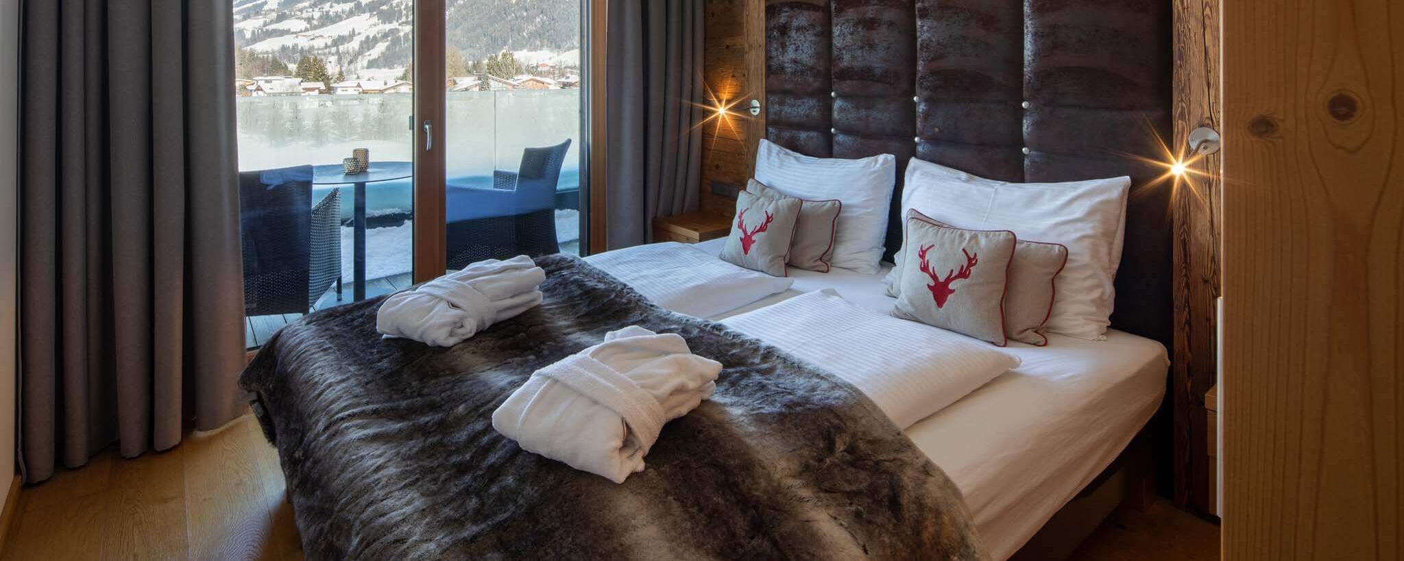 Doppelbett mit Fellplaid, Bademänteln und Blick auf den Balkon im Family Apartment im Bergresort Westendorf