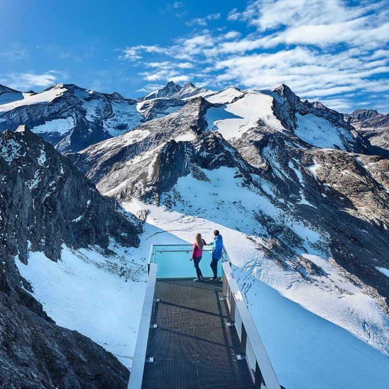 Pärchen blickt von einer Panoramaplattform auf den Großglockner und weitere 3.000er der Hohen Tauern.