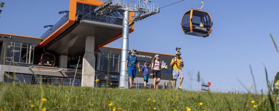 Familie beim Wandern am Kreischberg mit Sommerbergbahn im Hintergrund.