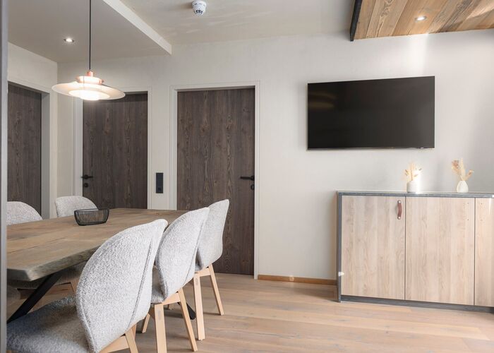 An apartment with a table and armchair, a wardrobe and a screen in the background.