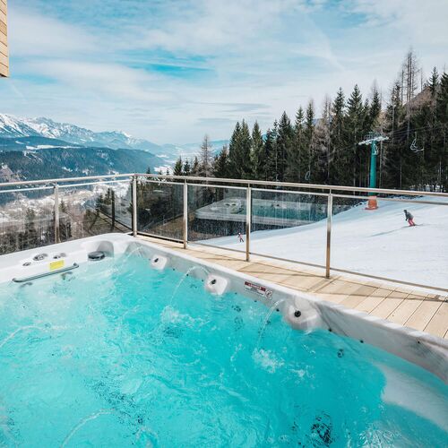 Außen Whirlpool auf der Terrasse eines Chalets der Alpenchalets Reiteralm mit Blick auf die verschneite Landschaft