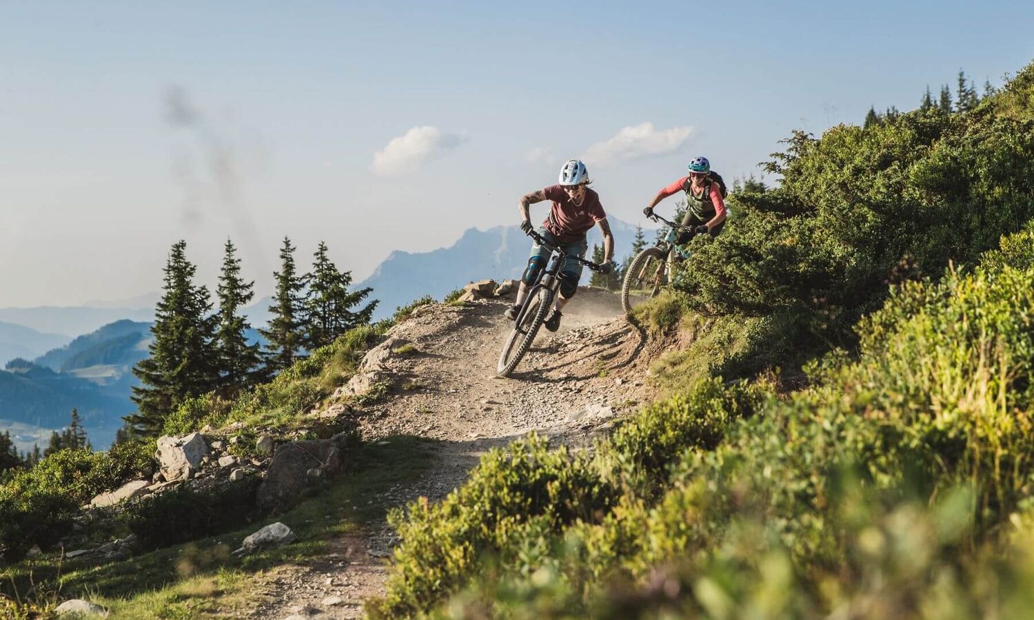 Twee downhillbikers razen over een alpien parcours, omringd door indrukwekkend berglandschap